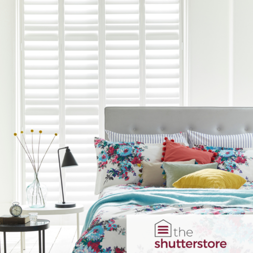 Bed with colourful fabrics and large white shutters in the background